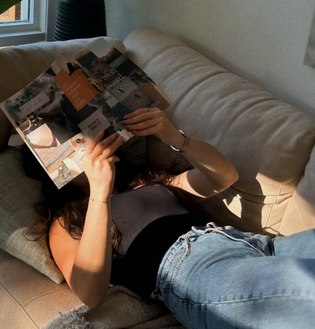  Woman lounging on a couch while reading a vision board book filled with moodboard-style images and quotes.