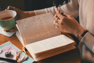  Woman journaling in a cozy café setting with handwritten pages, a warm drink, crystals, and pastel stationery laid out on the table.